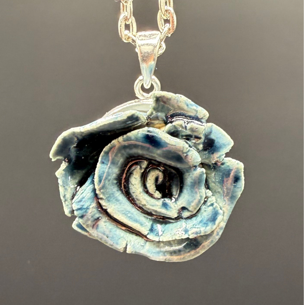 Silver rose-shaped pendant on a chain against a gray background