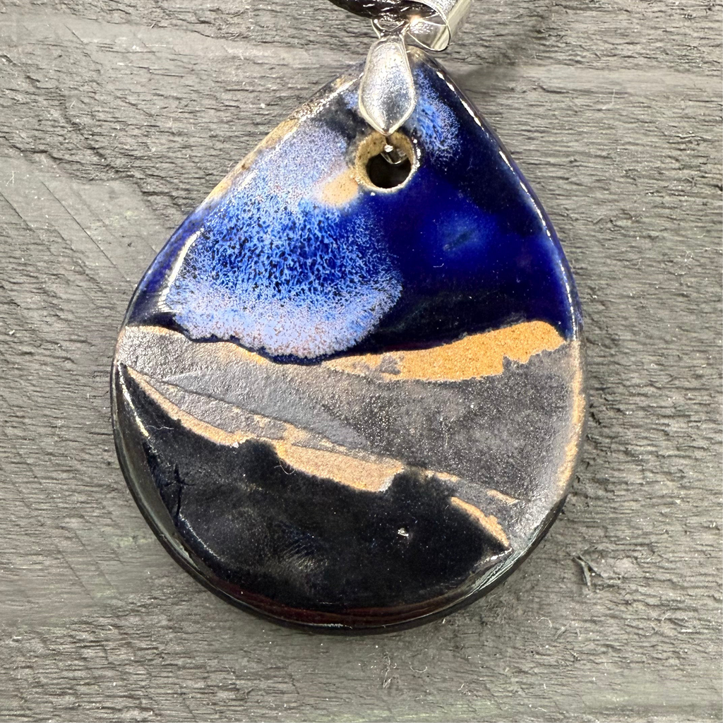 Teardrop-shaped pendant with blue, gold, and black design on a gray surface