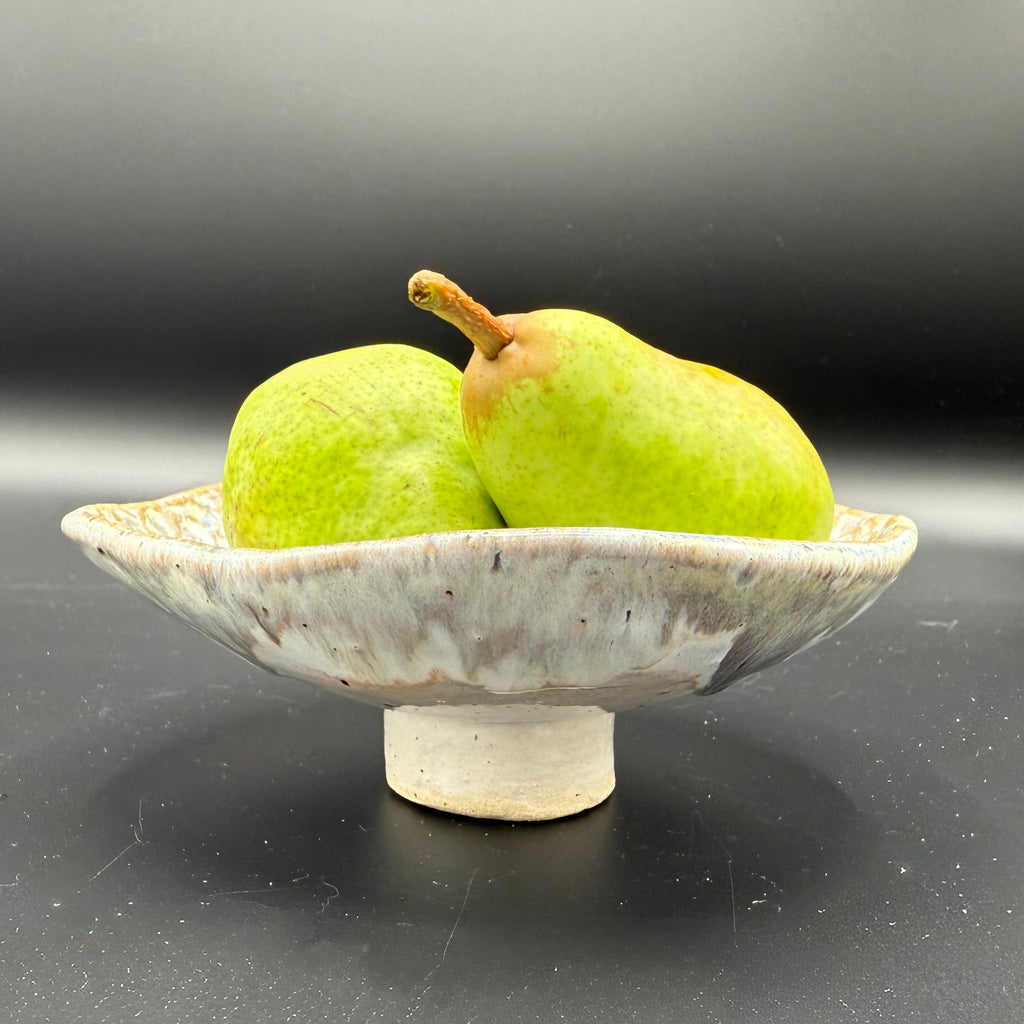 Two green pears on a small ceramic dish with a dark background