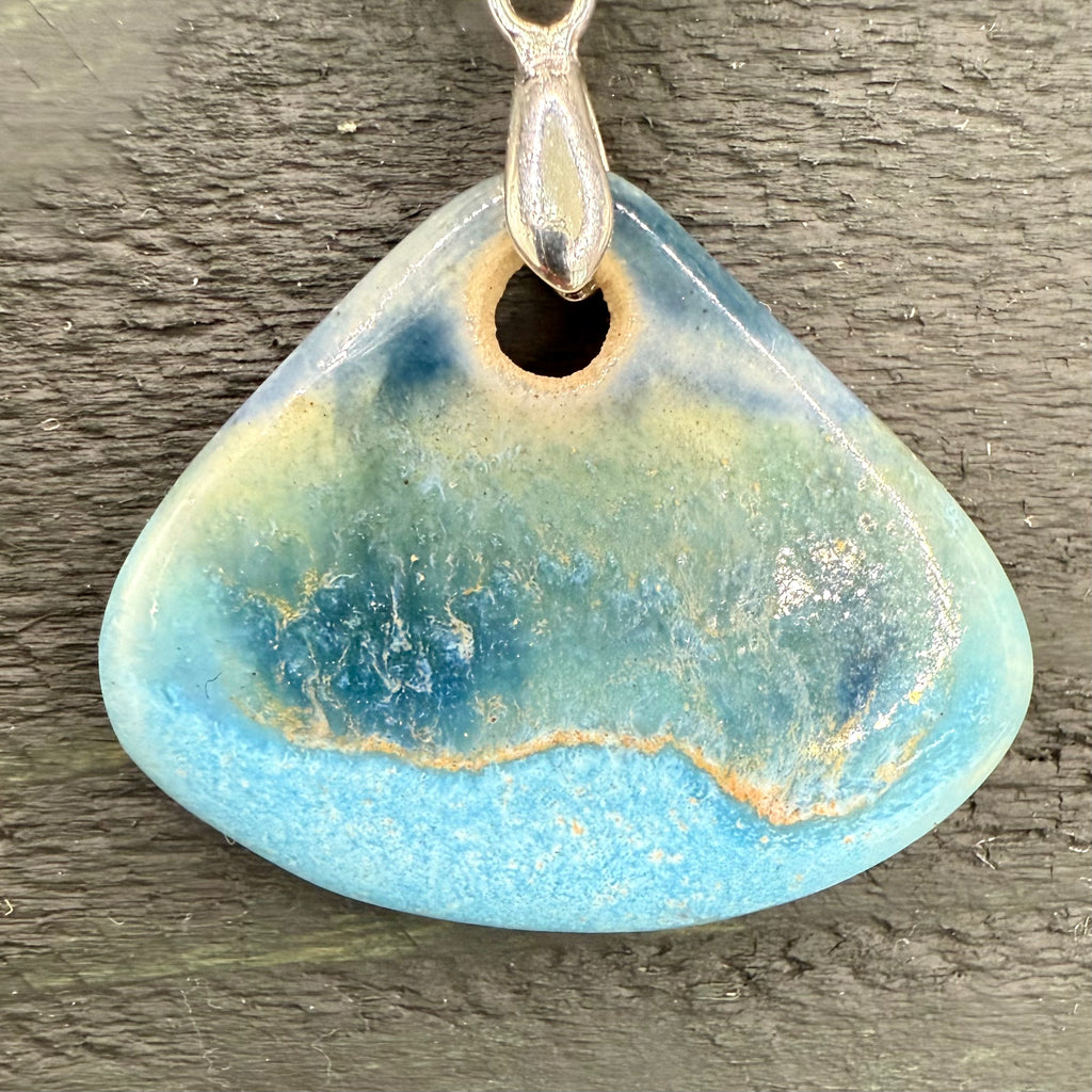 Triangular blue sea pendant with a silver hook on a wooden surface