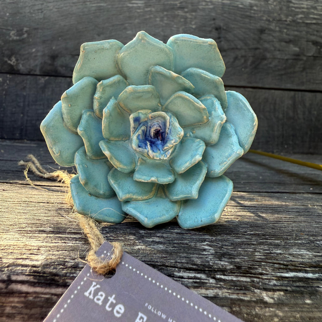Blue ceramic succulent flower on a wooden surface with a tag l