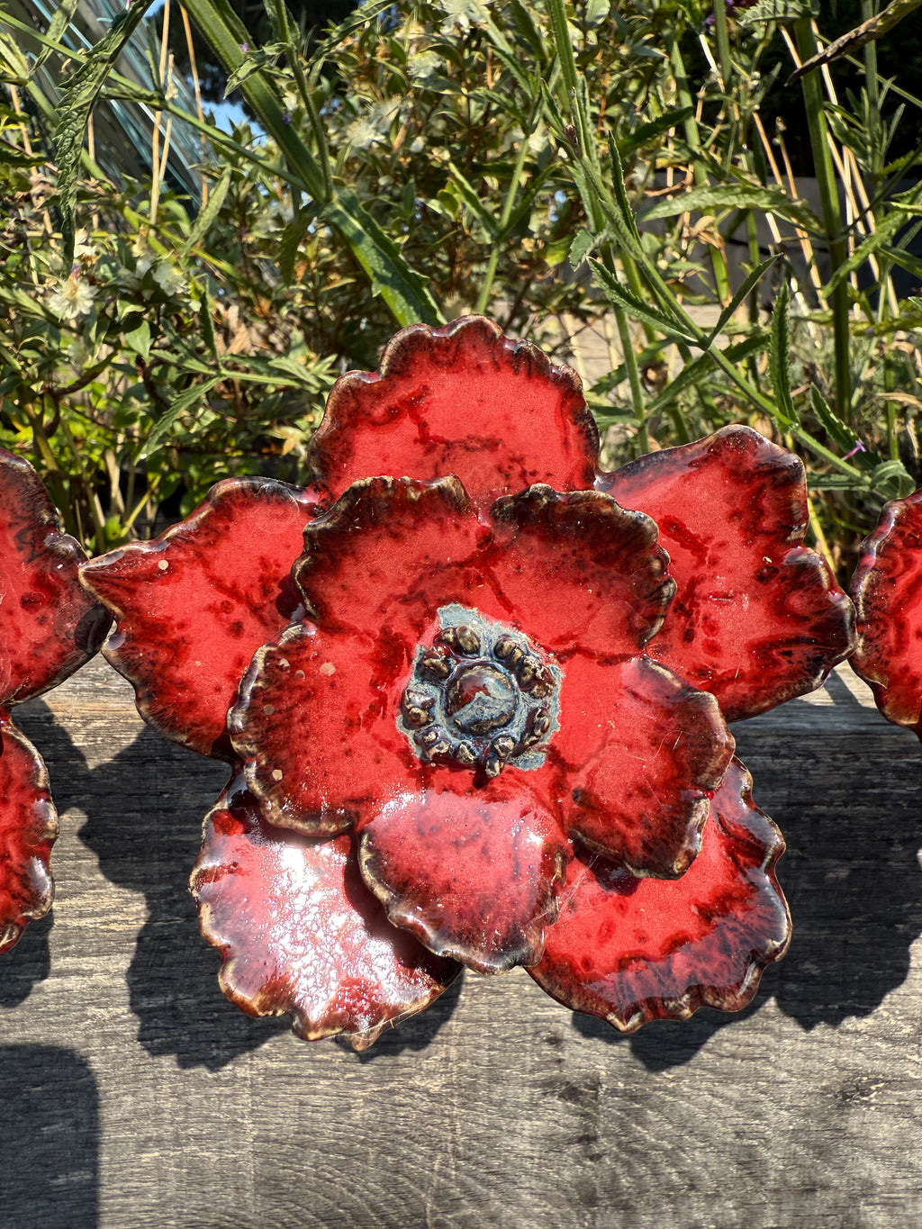 Red ceramic flower-shaped objects on a wooden surface with greenery in the background