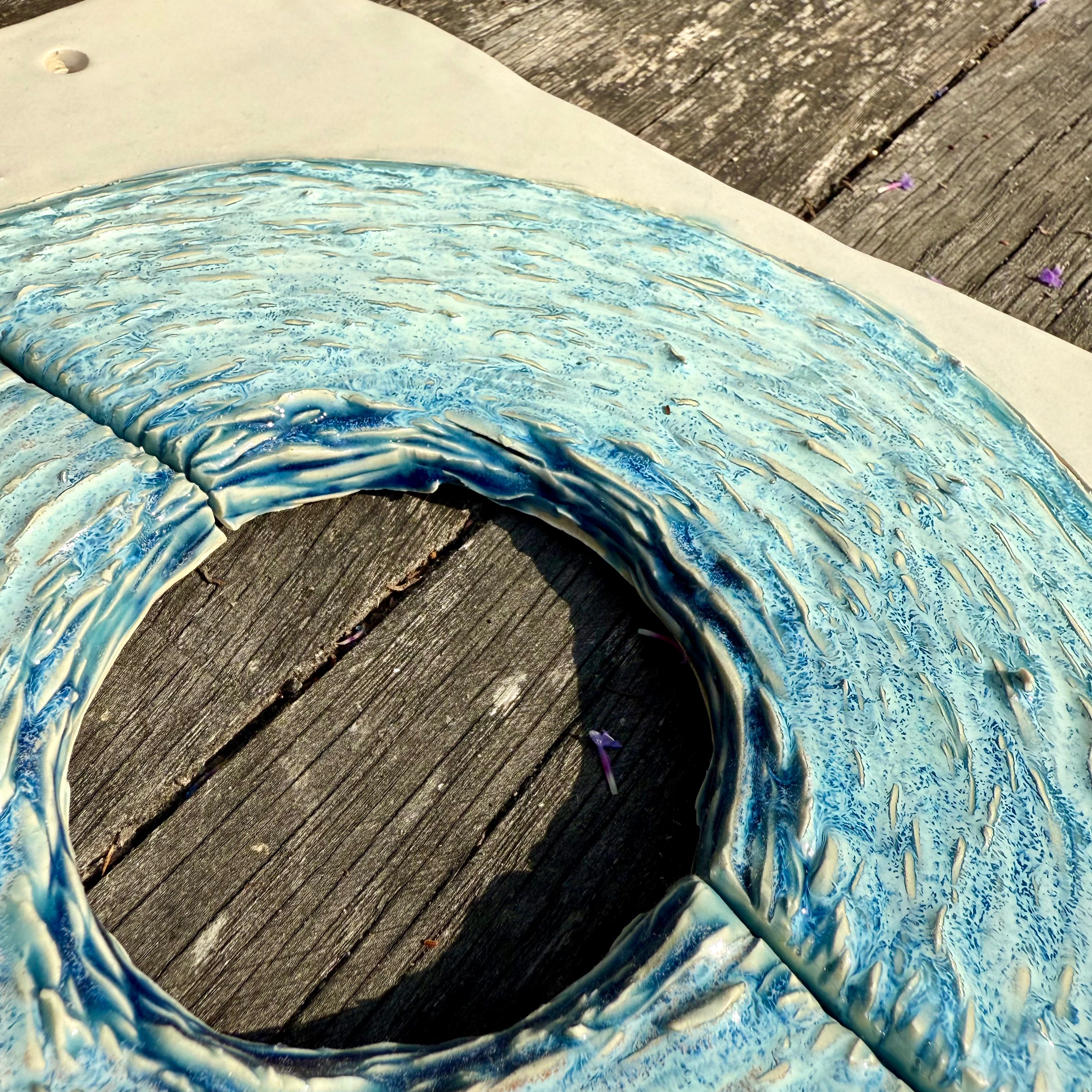 Circular hole in a blue and white ceramic textured surface with wooden background