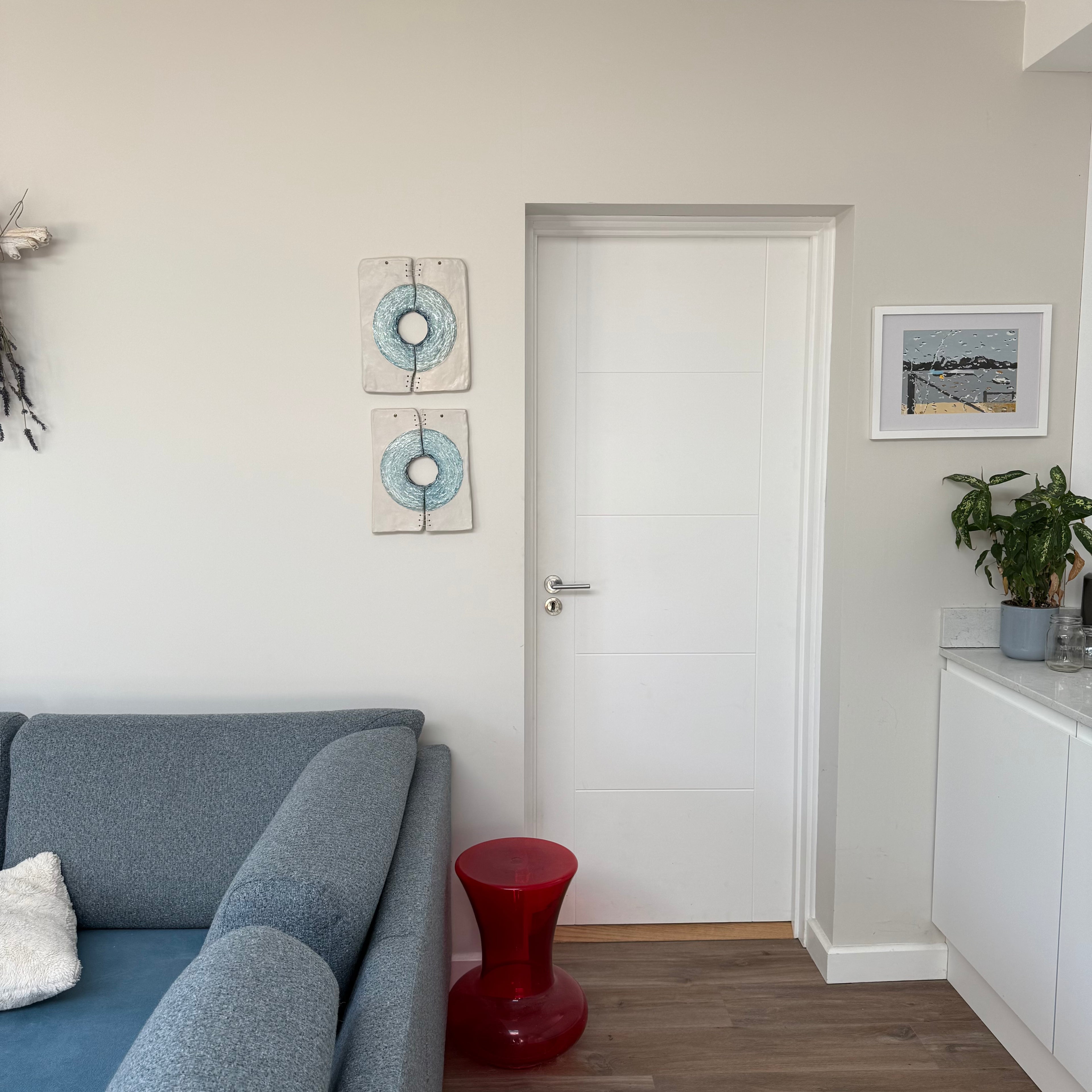 Modern living room with gray sofa, red stool, and white walls.
