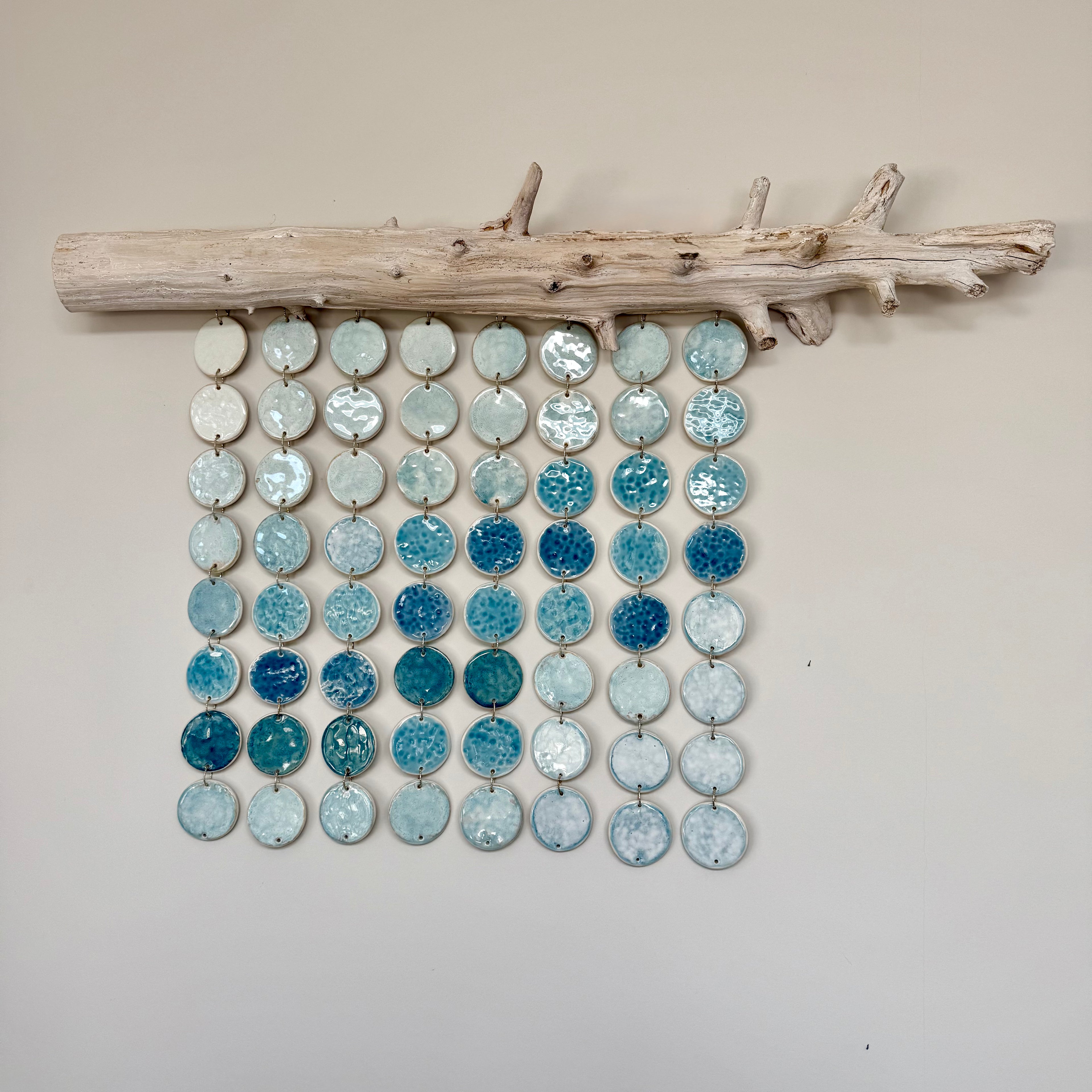 Decorative wall art with blue and white circular stones on a wooden branch against a beige wall.
