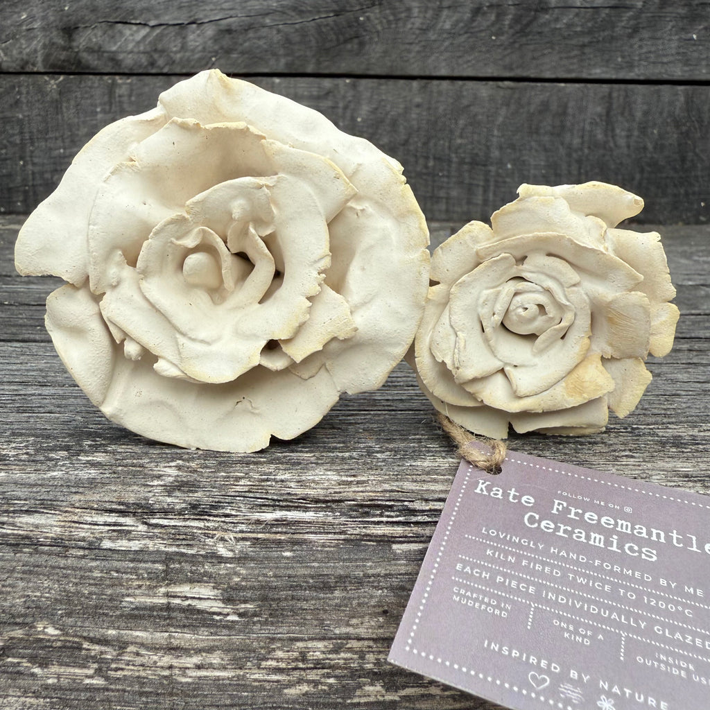 Two ceramic roses on a wooden surface with a label for Kate Freemantle Ceramics.