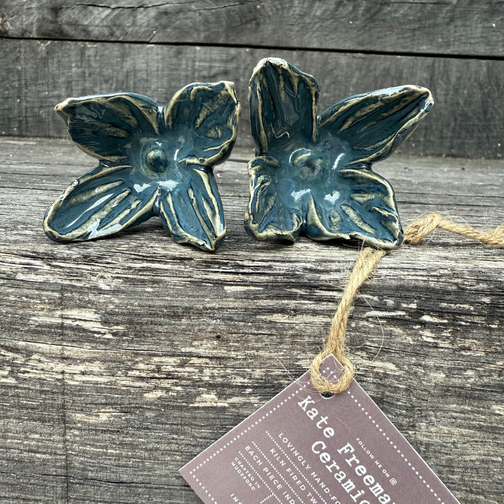 Two ceramic flower-shaped wall with metal stems on a wooden surface with a tag indicating 'Kate Freeman Ceramics'.
